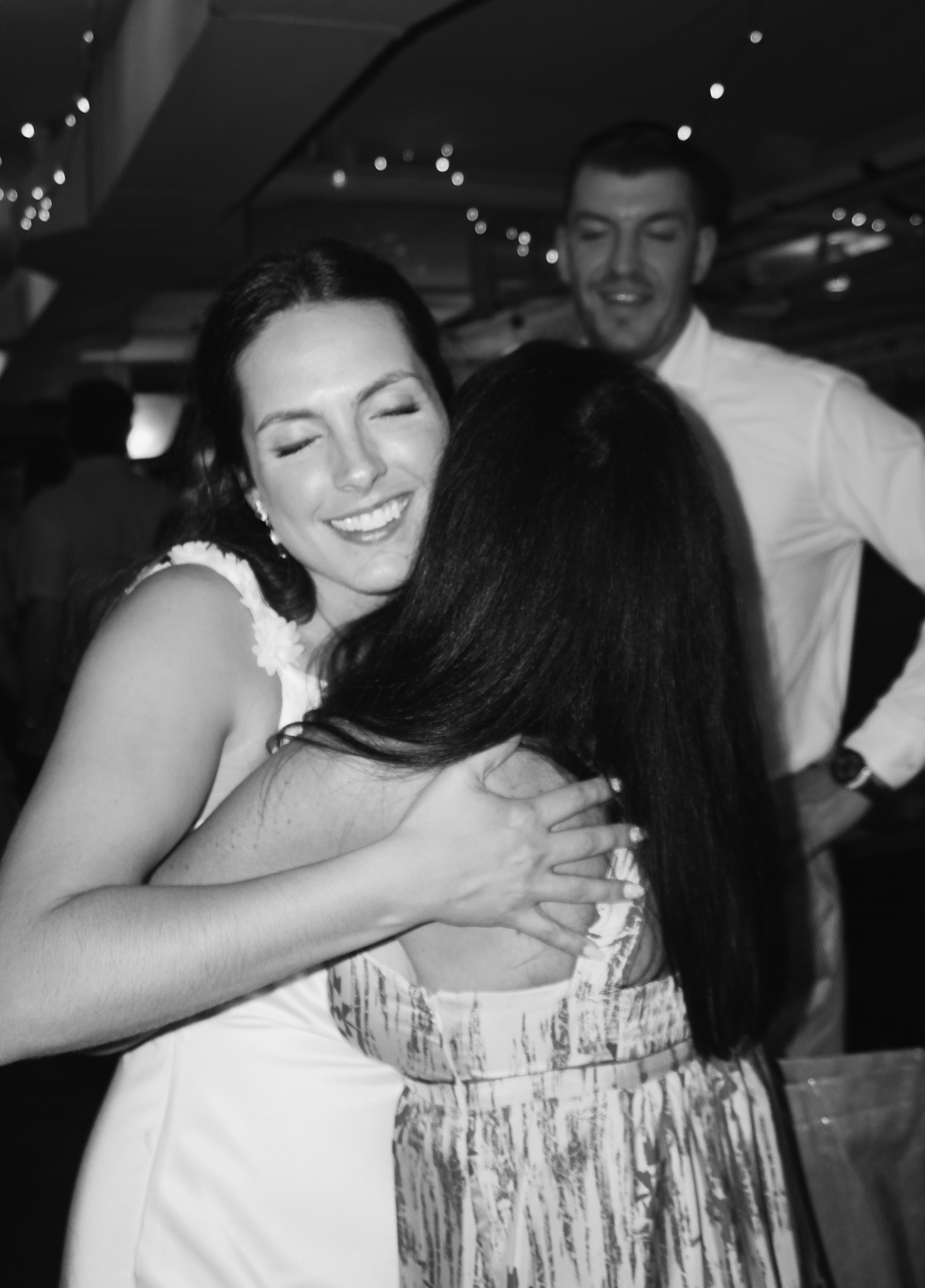 Black and white image of a bride hugging a friend at a wedding reception