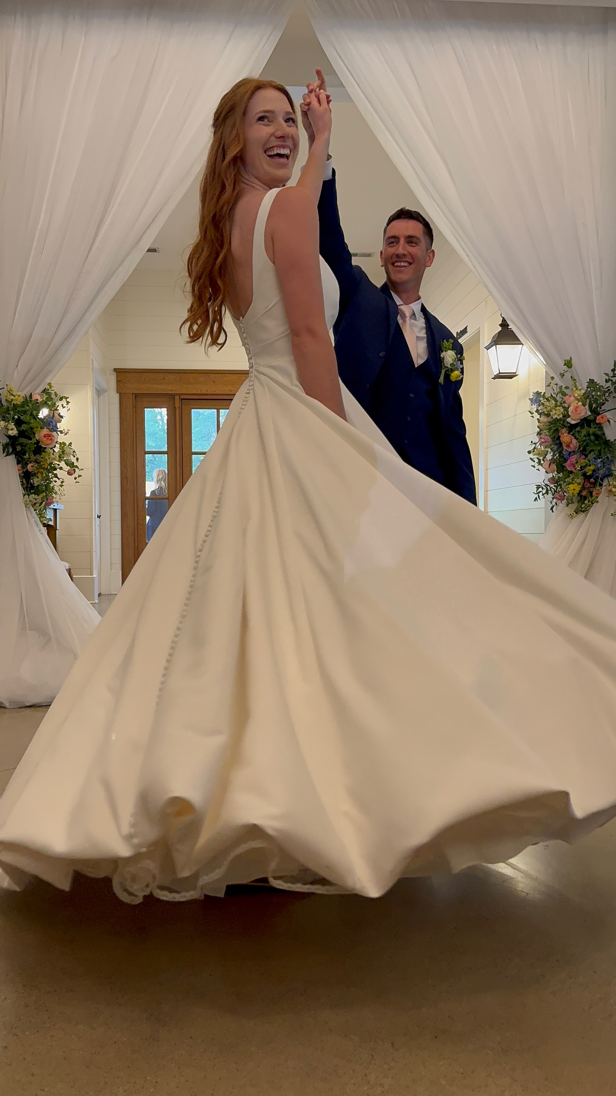 A bride twirling in her wedding dress with her groom in the background